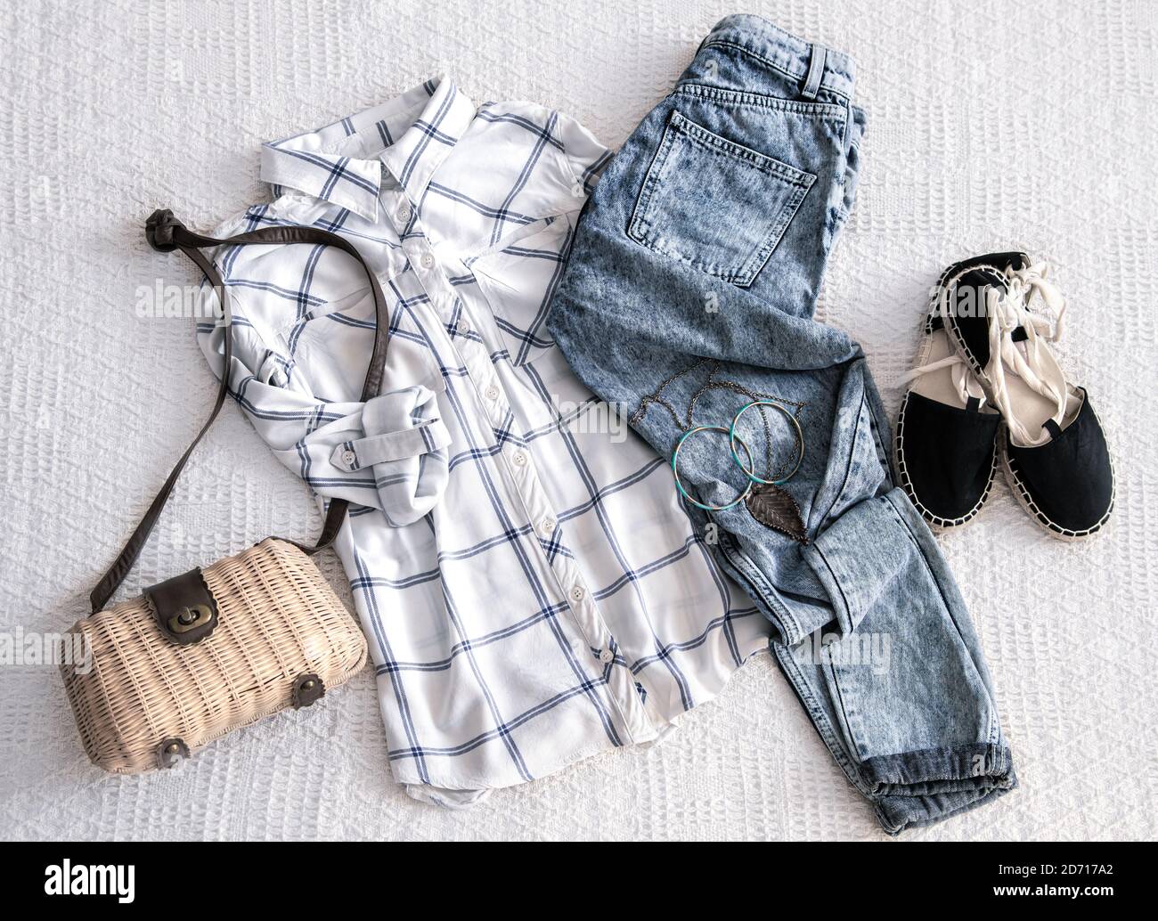 Conjunto con ropa de moda para mujer, camisa, jeans y bolsa con accesorios.  Sobre un fondo de tela ligera. Vista superior. Look moderno de cintura  baja. Lay plano Fotografía de stock -