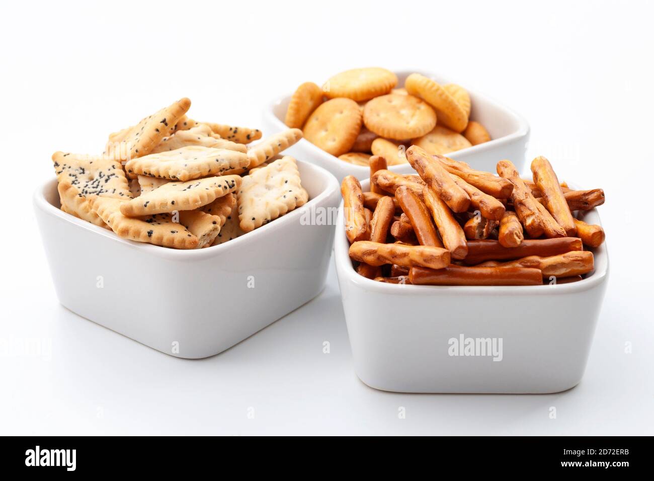 Selección de pretzels, palitos, galletas saladas y bocadillos salados en cuencos blancos de cerámica aislados sobre fondo blanco Foto de stock