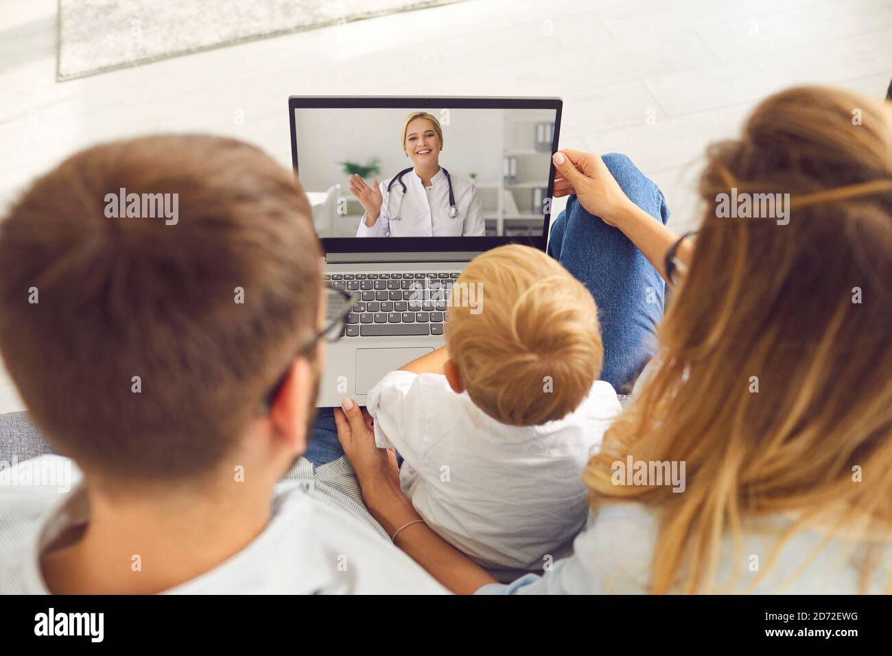 La familia joven con un hijo hace una llamada de video vía computadora portátil a un pediatra para que le aconseje y asesore. Foto de stock
