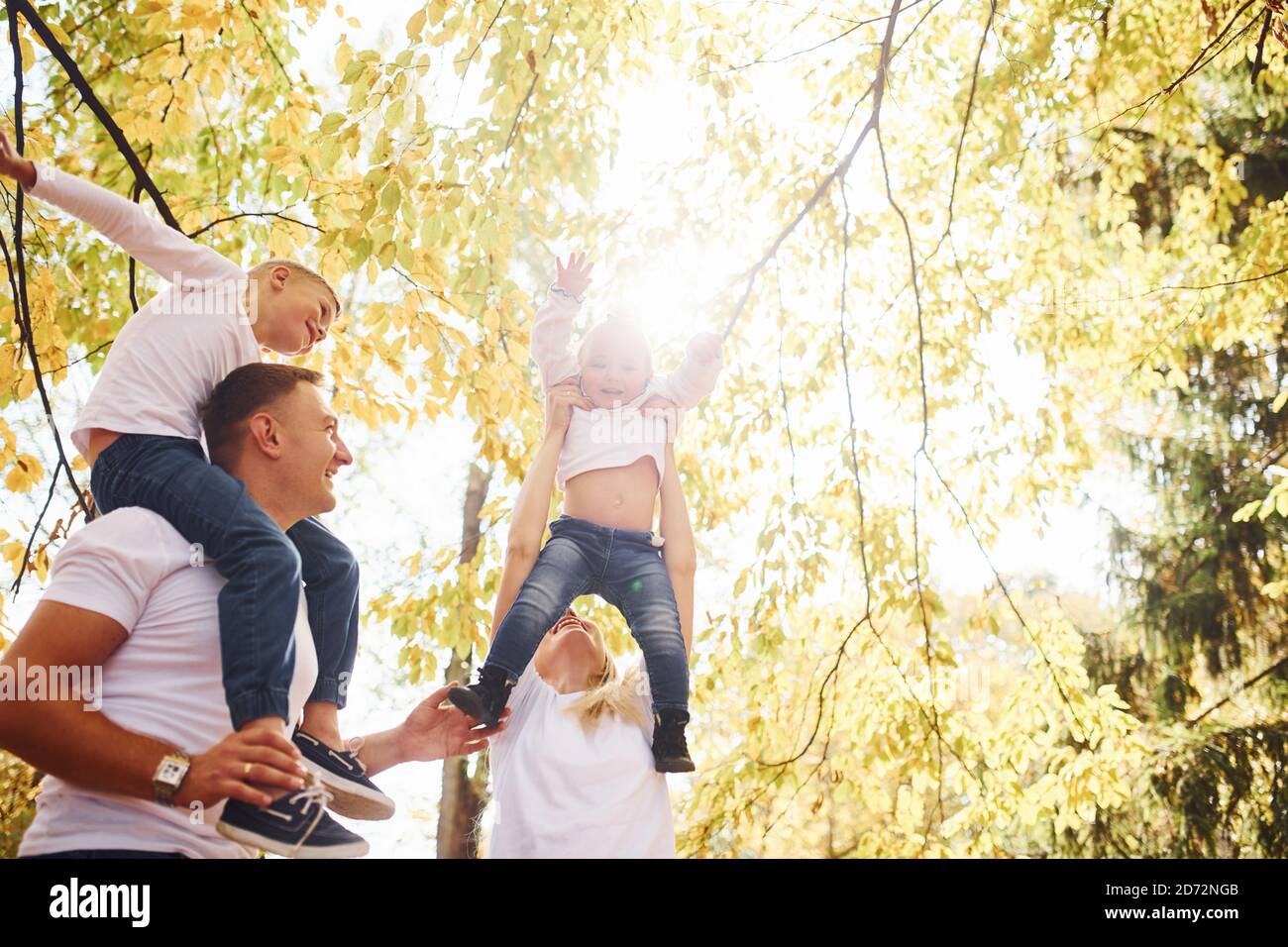 La madre y el papá mantienen a los niños en los hombros y en las manos. Alegre familia joven tienen un paseo juntos en un parque de otoño Foto de stock