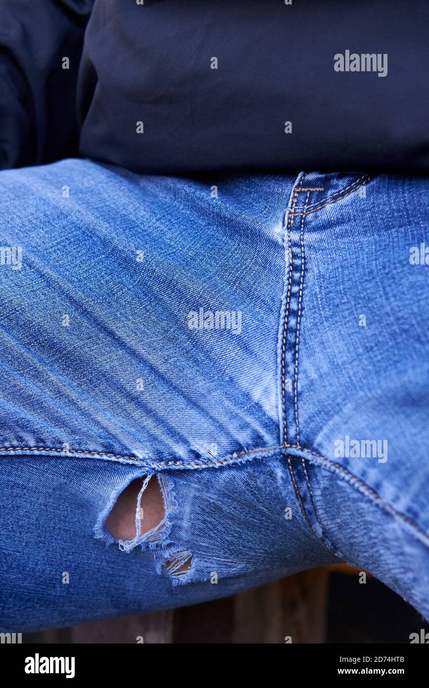 Jeans envejecidos con agujeros entre las piernas de un hombre gordo, primer plano. Foto de stock