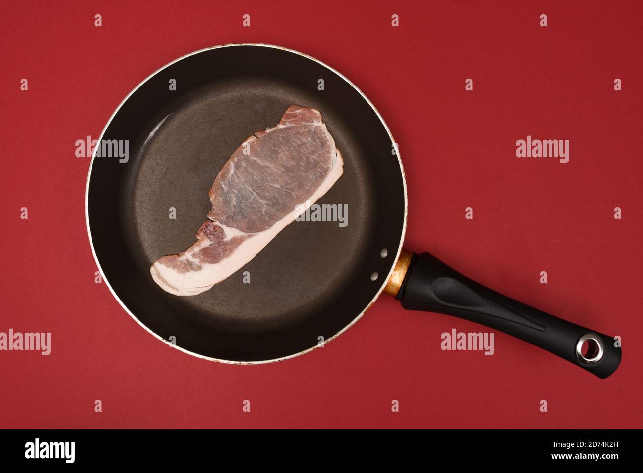 un rasher de bacon crudo en una sartén aislado sobre fondo rojo Foto de stock