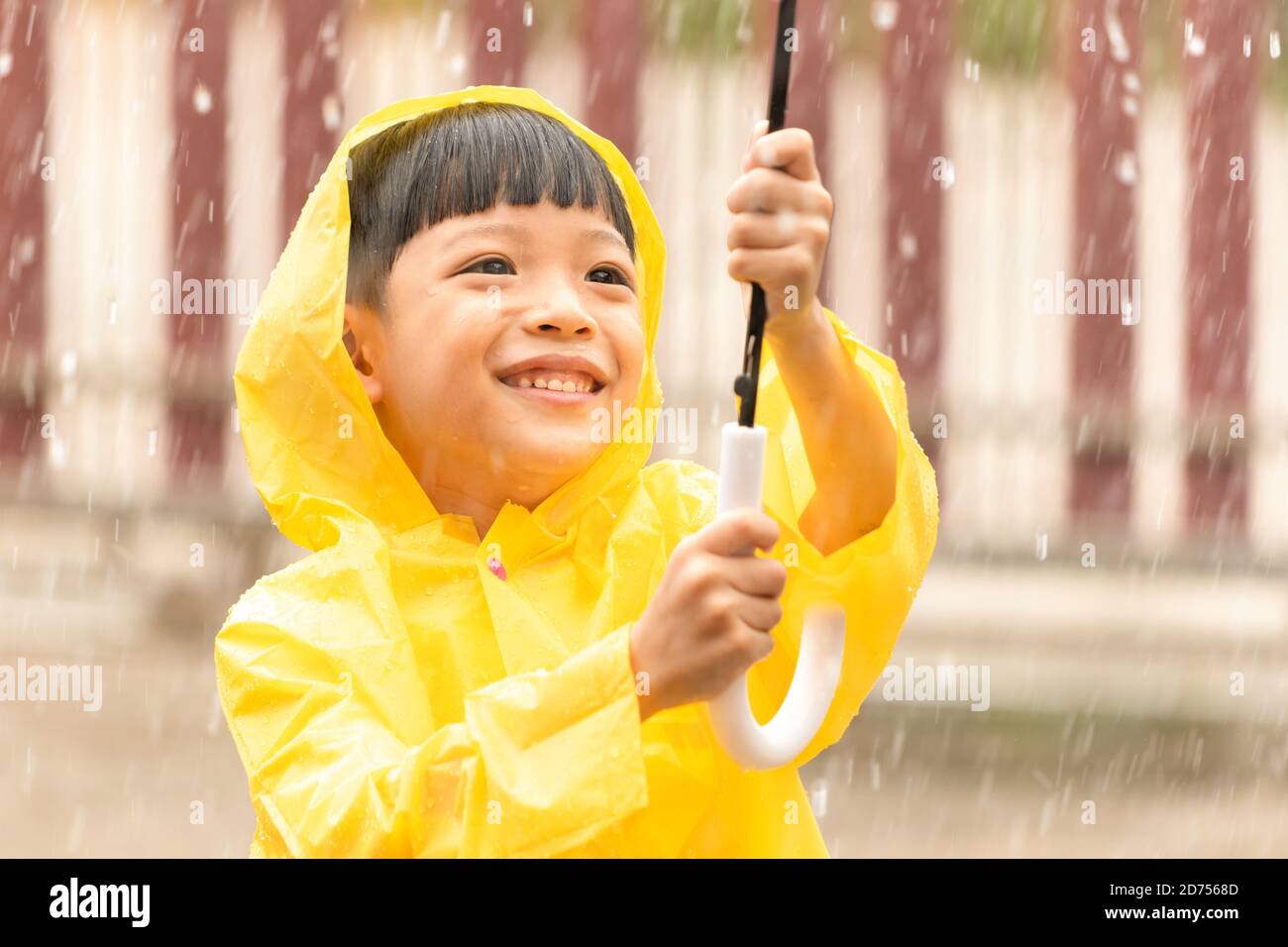 Niño asiático feliz sosteniendo un paraguas que se divierte jugando con los raindrops. Un chico con un impermeable amarillo. Foto de stock