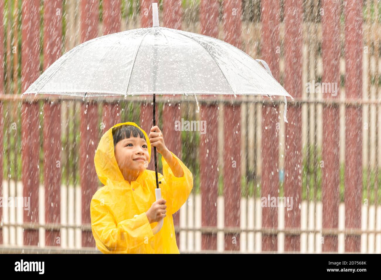 Niño asiático feliz sosteniendo un paraguas que se divierte jugando con los raindrops. Un chico con un impermeable amarillo. Foto de stock