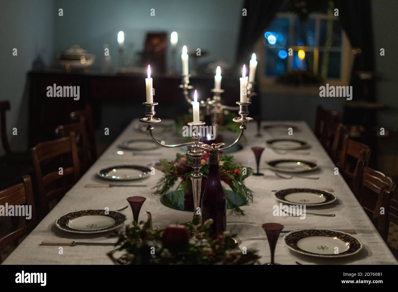Una mesa de comedor formal romántico y oscuro con platos de porcelana vintage, candelabros de plata con velas encendidas blancas, un mantel blanco, floral Foto de stock