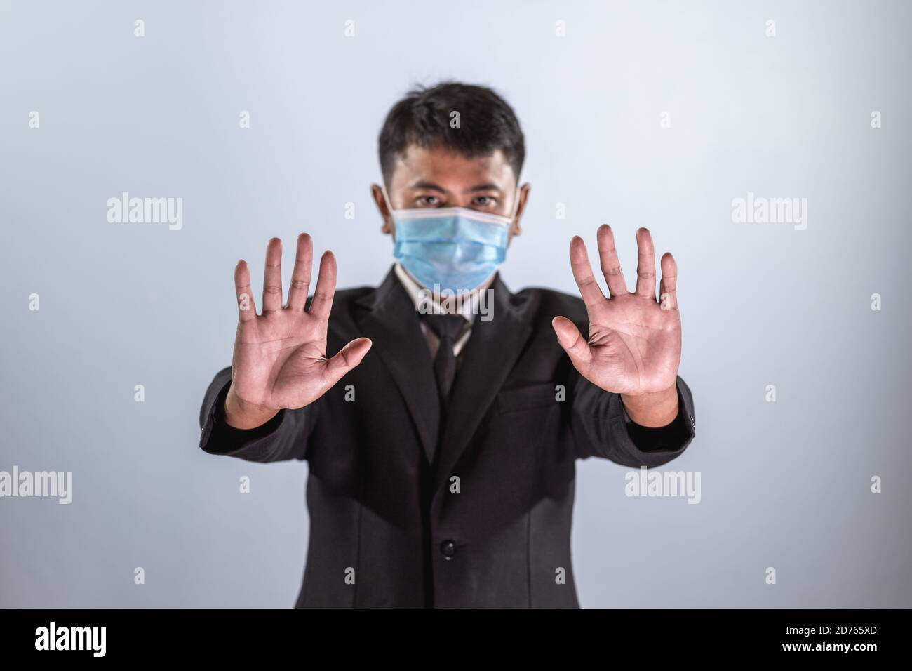 Los empresarios asiáticos usan una máscara para prevenir la enfermedad del coronavirus y muestran el signo de mano para detener el coronavirus. Foto de stock