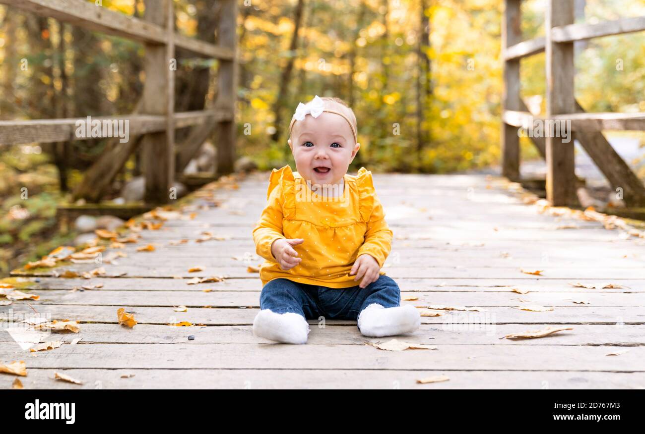 el bebé se sienta en el puente con las hojas de arce otoño cerca Foto de stock