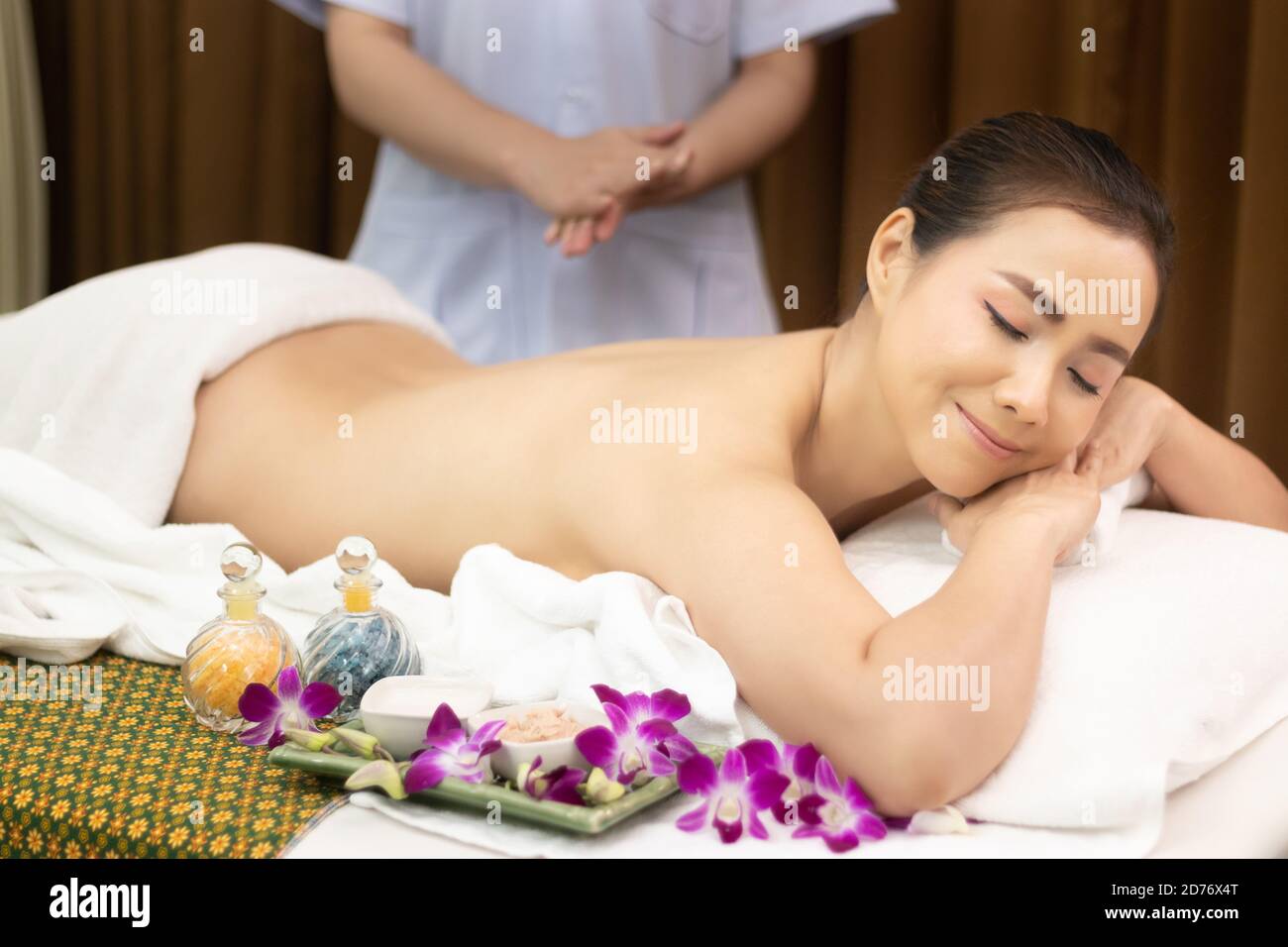 Hermosa joven relajarse mujer asiática tumbada en la cama de masaje con cuerpo desnudo, masseur preparar masaje de aceite en la parte trasera en el tratamiento de belleza spa salón Foto de stock