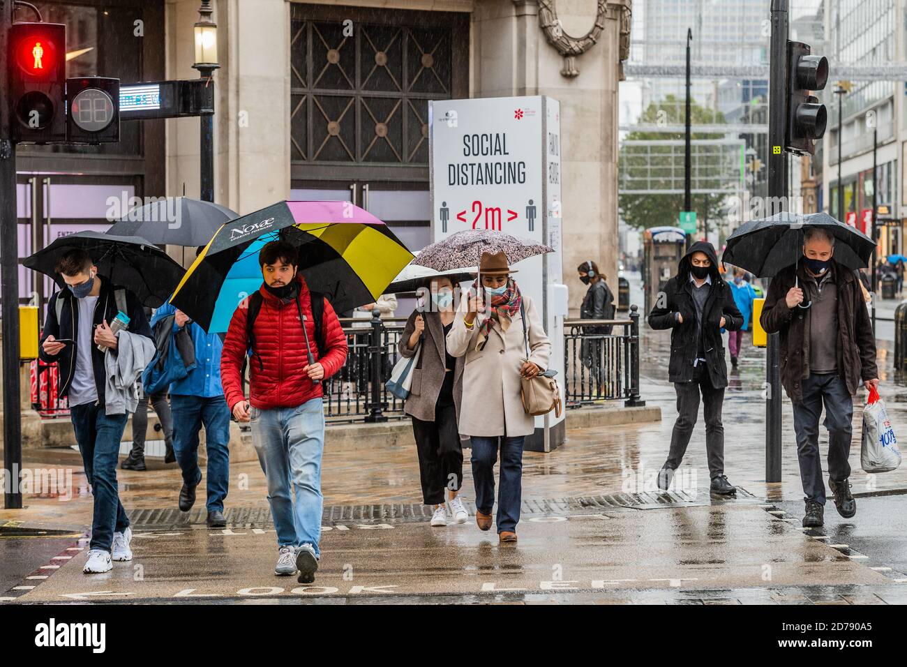Londres, Reino Unido. 21 de octubre de 2020. Los paraguas están humedecidos espíritus en Oxford Street, ya que los signos de mantener 2 m recuerdan a la gente sobre el distanciamiento social. Los tiempos difíciles para los minoristas como el como la lluvia cae y las restricciones de Coronavirus comienzan a aumentar de nuevo. Crédito: Guy Bell/Alamy Live News Foto de stock