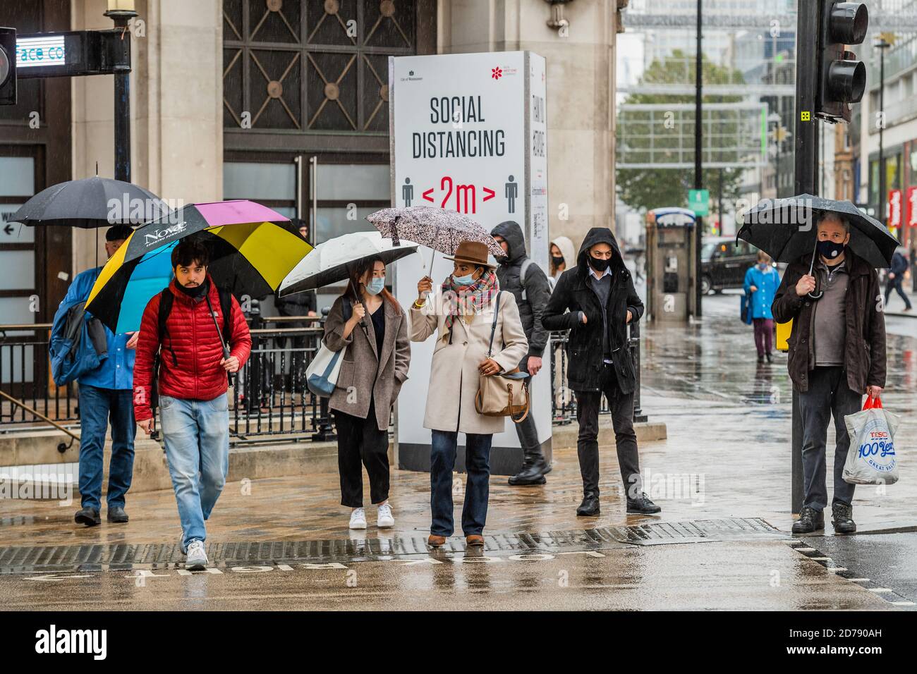 Londres, Reino Unido. 21 de octubre de 2020. Los paraguas están humedecidos espíritus en Oxford Street, ya que los signos de mantener 2 m recuerdan a la gente sobre el distanciamiento social. Los tiempos difíciles para los minoristas como el como la lluvia cae y las restricciones de Coronavirus comienzan a aumentar de nuevo. Crédito: Guy Bell/Alamy Live News Foto de stock