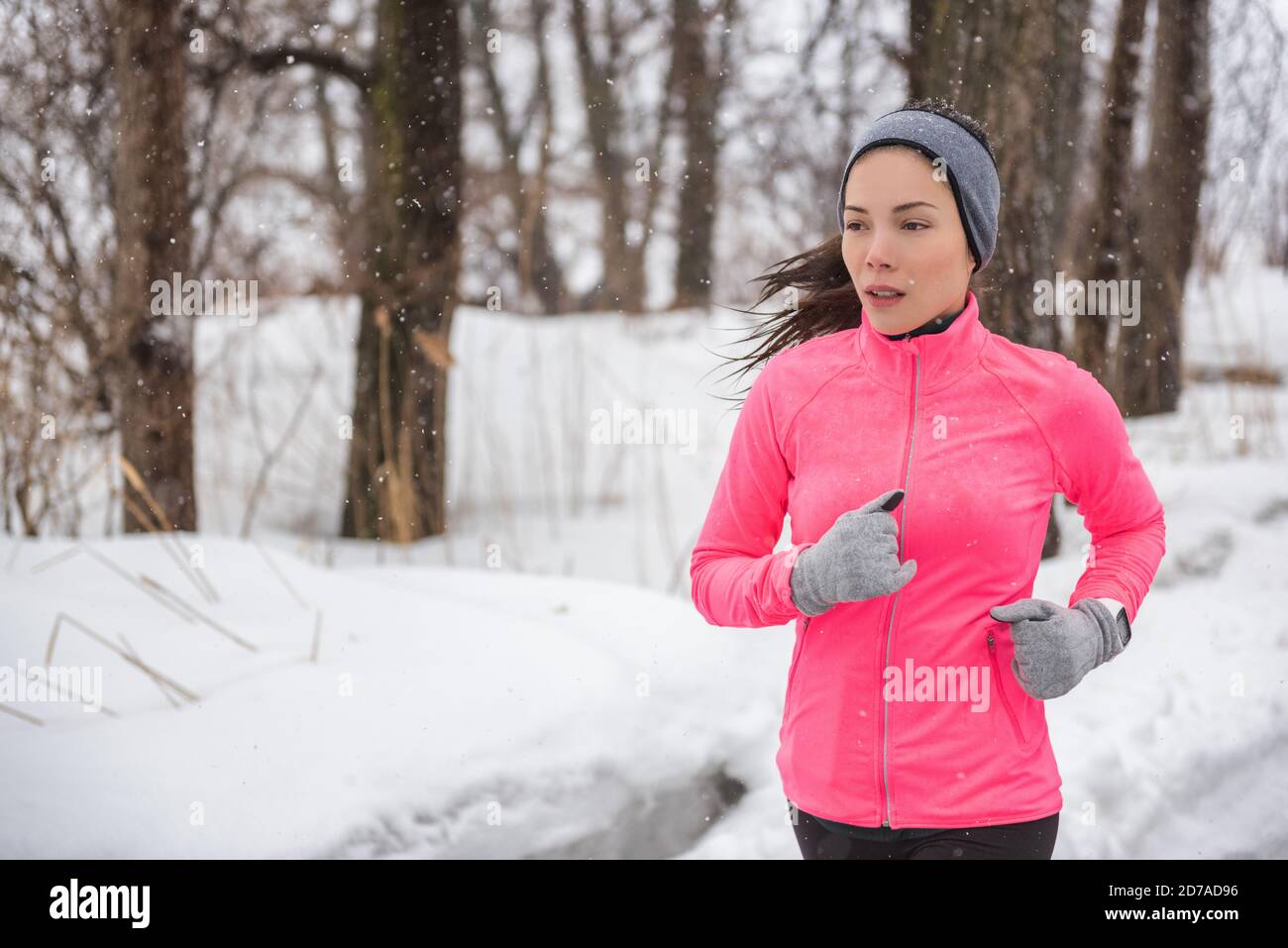 Deporte de invierno niña corriendo en la nieve usando chaqueta de viento,  guantes, cinta para la cabeza y smartwatch. Mujer asiática de entrenamiento  saludable y activo estilo de vida Fotografía de stock -