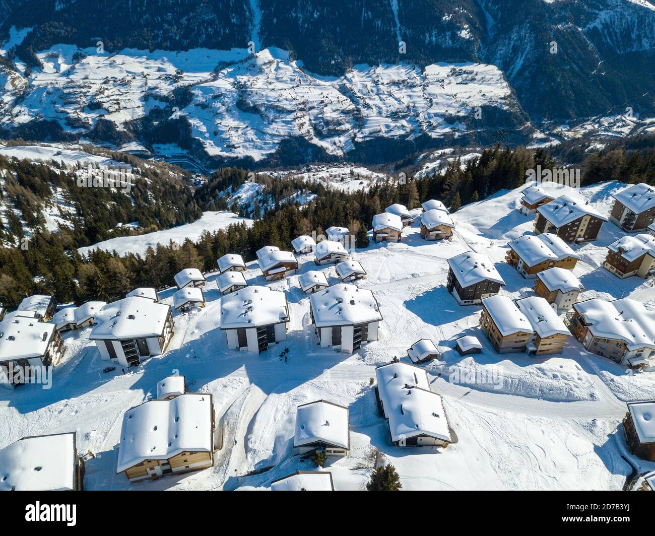 Vista aérea de los tejados cubiertos de nieve sobre los chalés tradicionales con estación de telesilla de esquí en el pueblo de los alpes suizos. Foto de stock