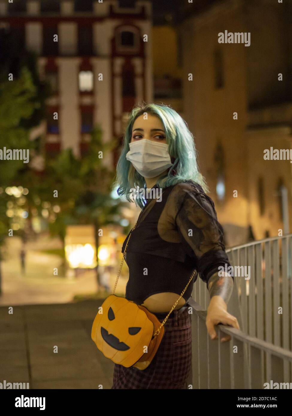 Enfoque poco profundo de una mujer con el cabello azul con un mascarilla y  un bolso en forma de calabaza por la noche Fotografía de stock - Alamy