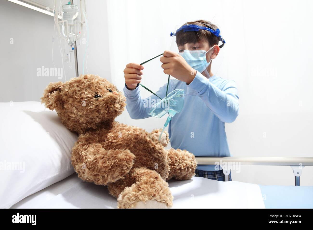 el niño del hospital coloca una mascarilla de oxígeno en el oso de peluche  sobre la cama, usando visera protectora y máscara quirúrgica, concepto de  protección de la corona virus covid 19
