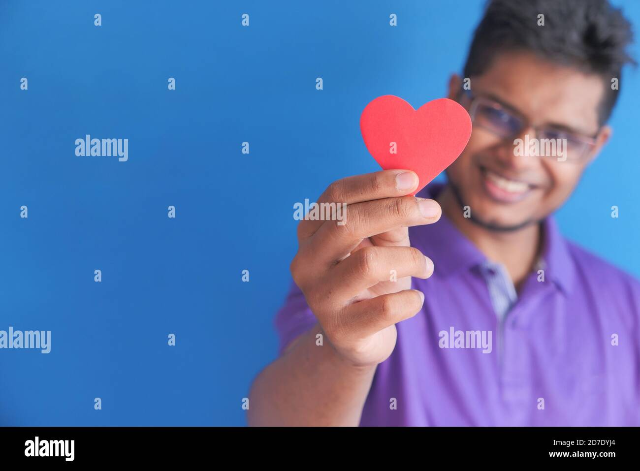 joven hombre feliz sosteniendo el corazón rojo sobre fondo azul Foto de stock