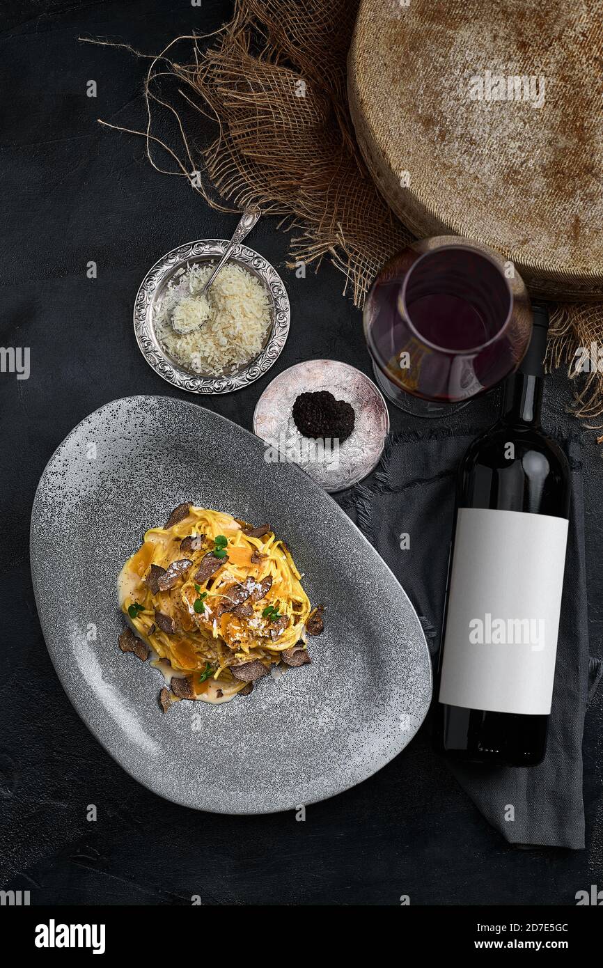 Cocina italiana - espaguetis con trufa negra en un plato gris y una botella de vino. Enfoque selectivo. Vertical. Foto de stock