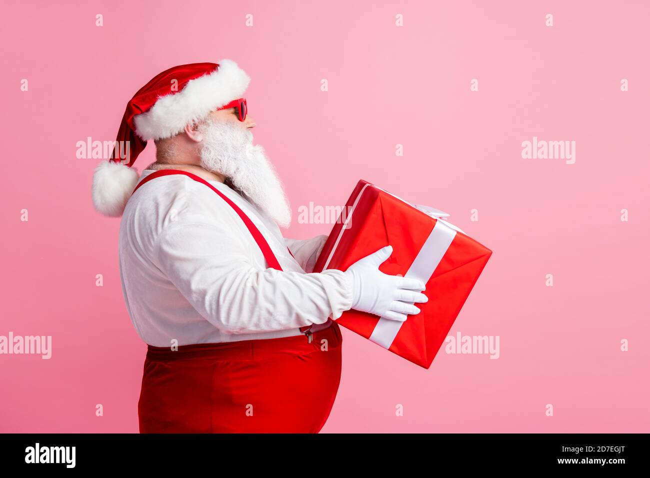 Perfil lado foto estilo claus polo norte trabajador entregar regalos noche de navidad mantener grande caja de regalo ropa de cabeza tapa de vidrio en general Fotografía de stock -