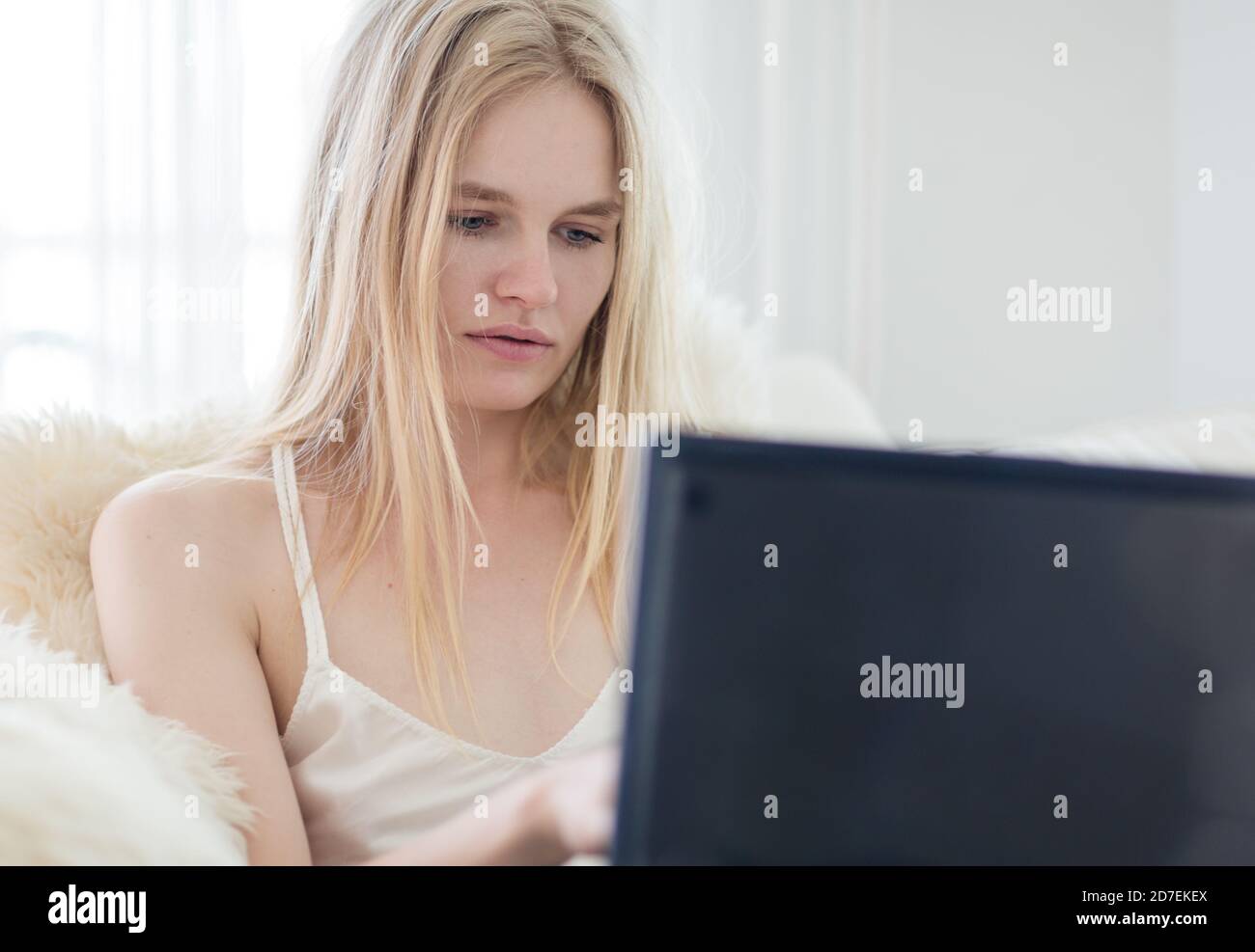 Mujer joven enfocada usando un ordenador portátil trabajando en línea desde casa. Foto de stock