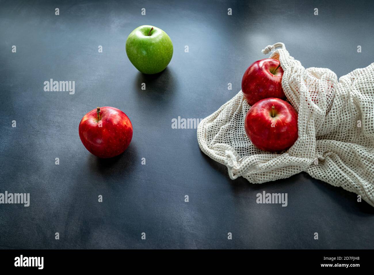 Manzanas rojas y verdes en una bolsa de malla de algodón sobre fondo oscuro. Concepto de compra de sostenibilidad y cero residuos. Vista superior Foto de stock