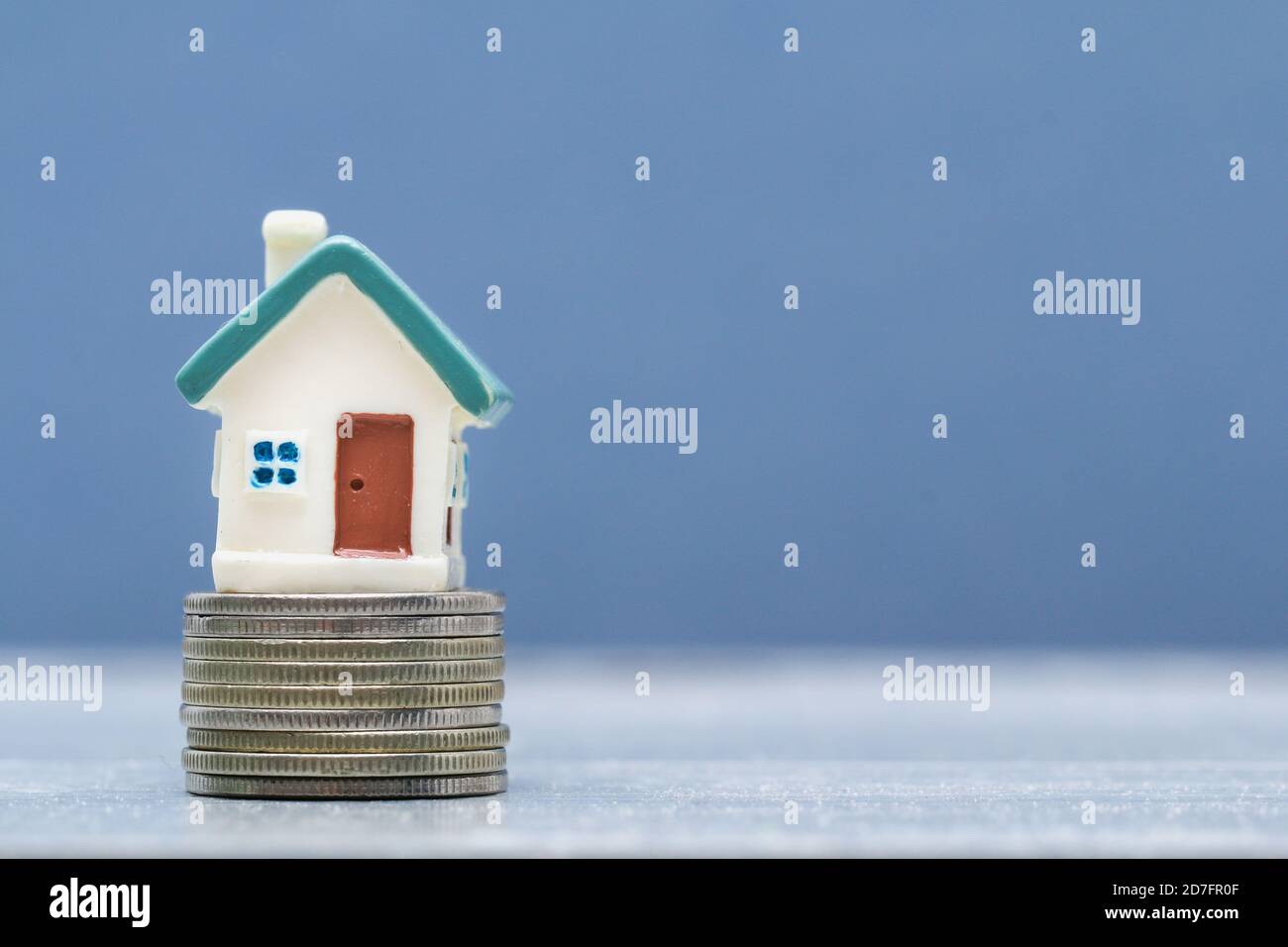 Pequeña casa de juguete en una pila de monedas sobre un fondo gris. Concepto de vivienda, hipoteca, préstamo. Foto de stock