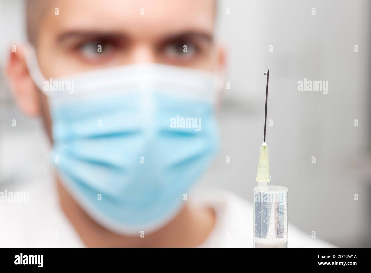 Primer plano del médico con mascarilla médica para la preparación de una jeringa vacunación - enfoque en la aguja Foto de stock