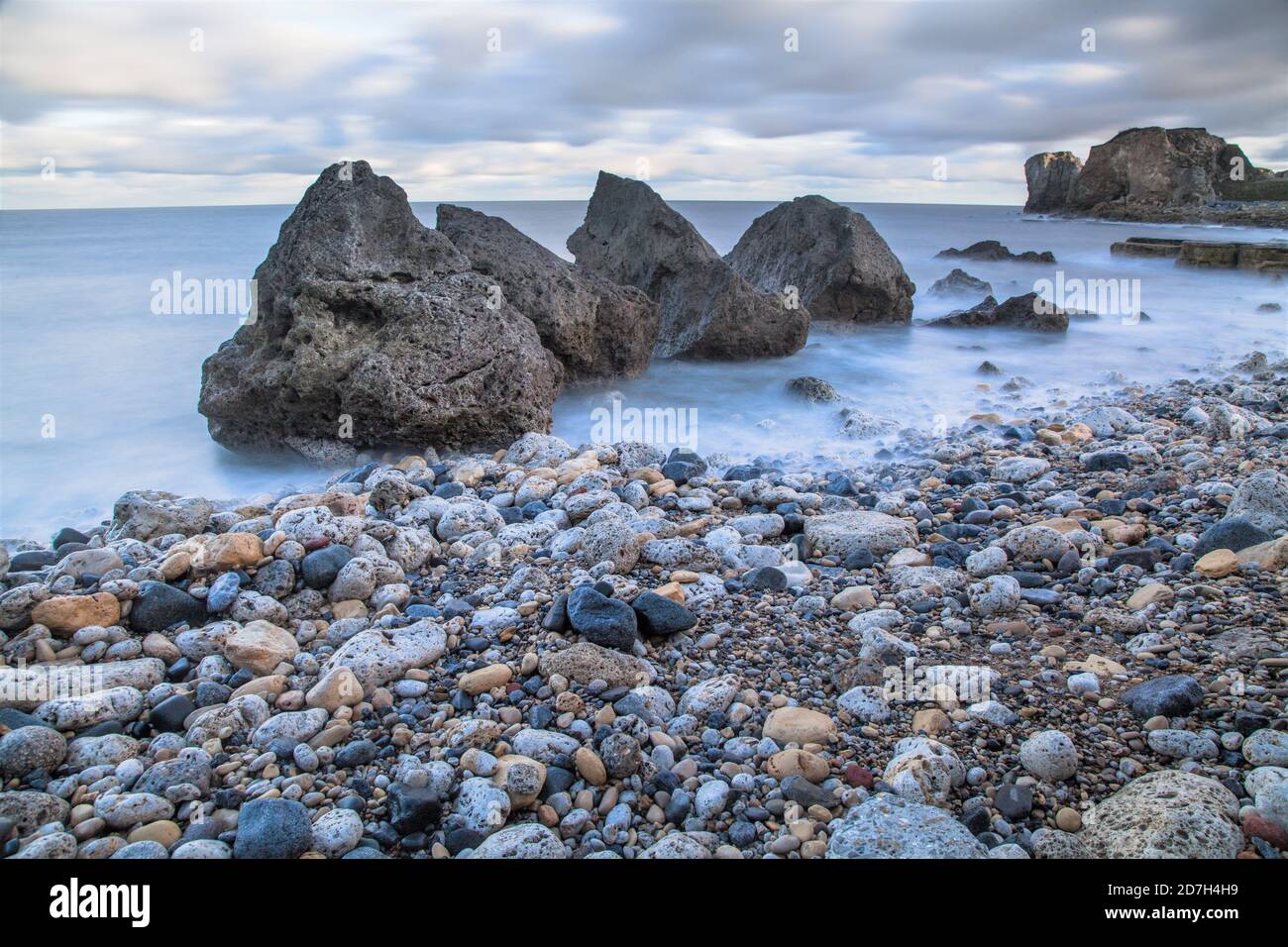 Olas que se deslizan alrededor de grandes rocas cerca de una playa de guijarros Foto de stock