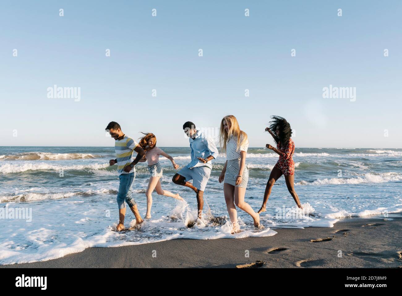 Jóvenes amigos jugando en el agua en la playa durante el día soleado Foto de stock