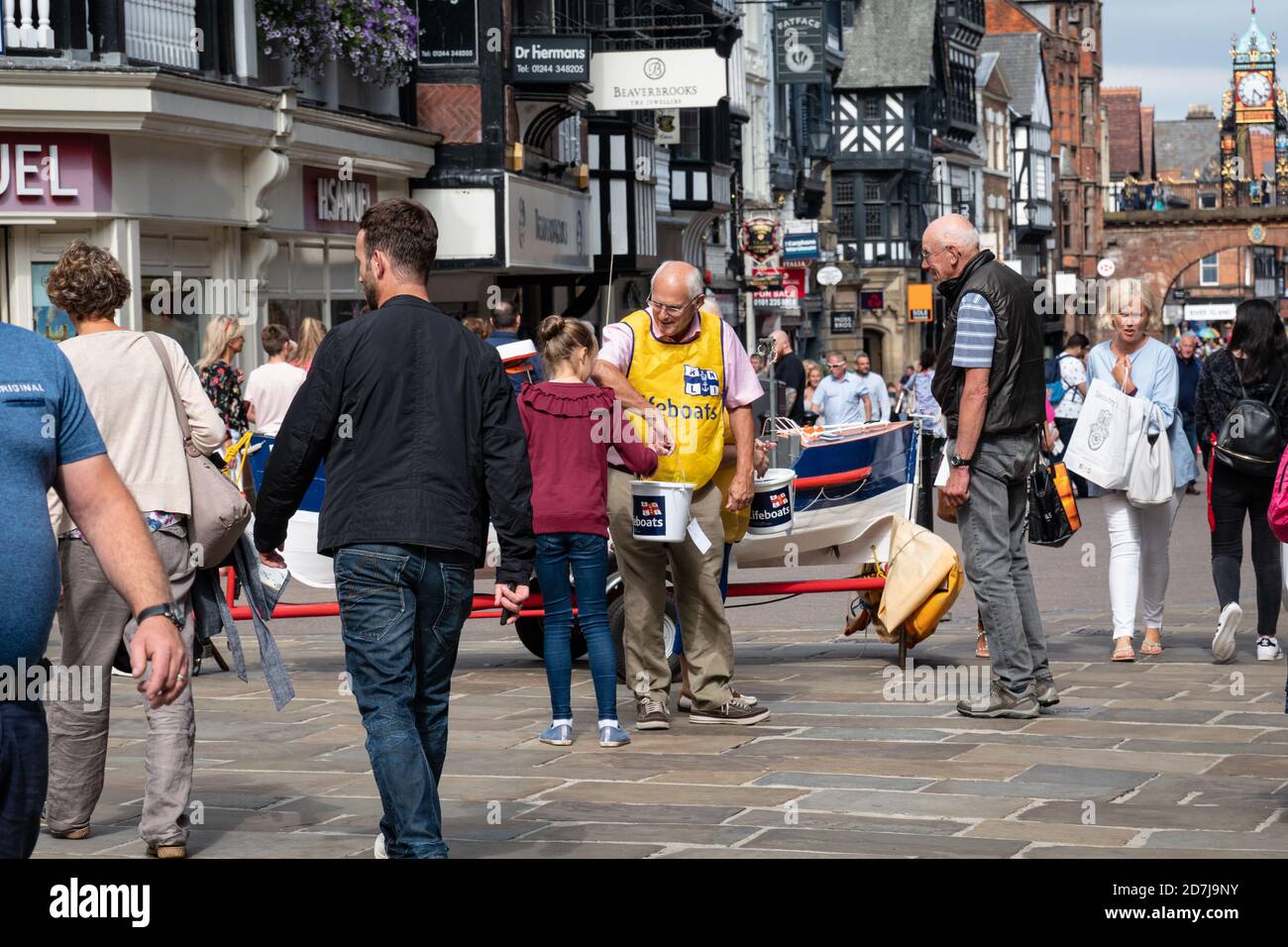 Chica haciendo una donación a RNLI en una calle ocupada Eastgate en Chester, Inglaterra Foto de stock