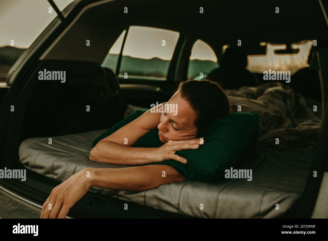 Mujer cansada durmiendo en el maletero del coche al atardecer Foto de stock