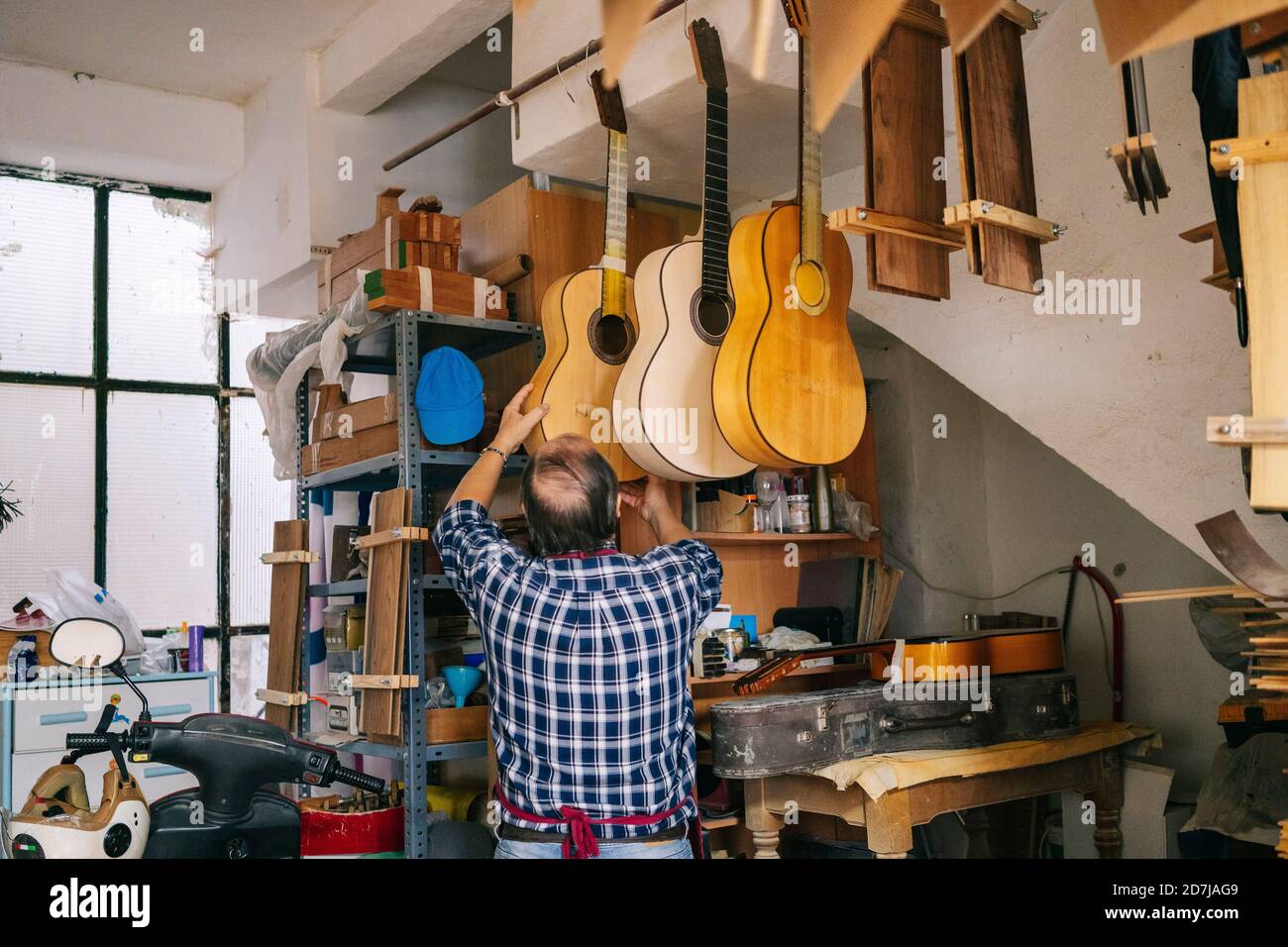 Hombre mayor colgando la guitarra en una línea en el taller Foto de stock