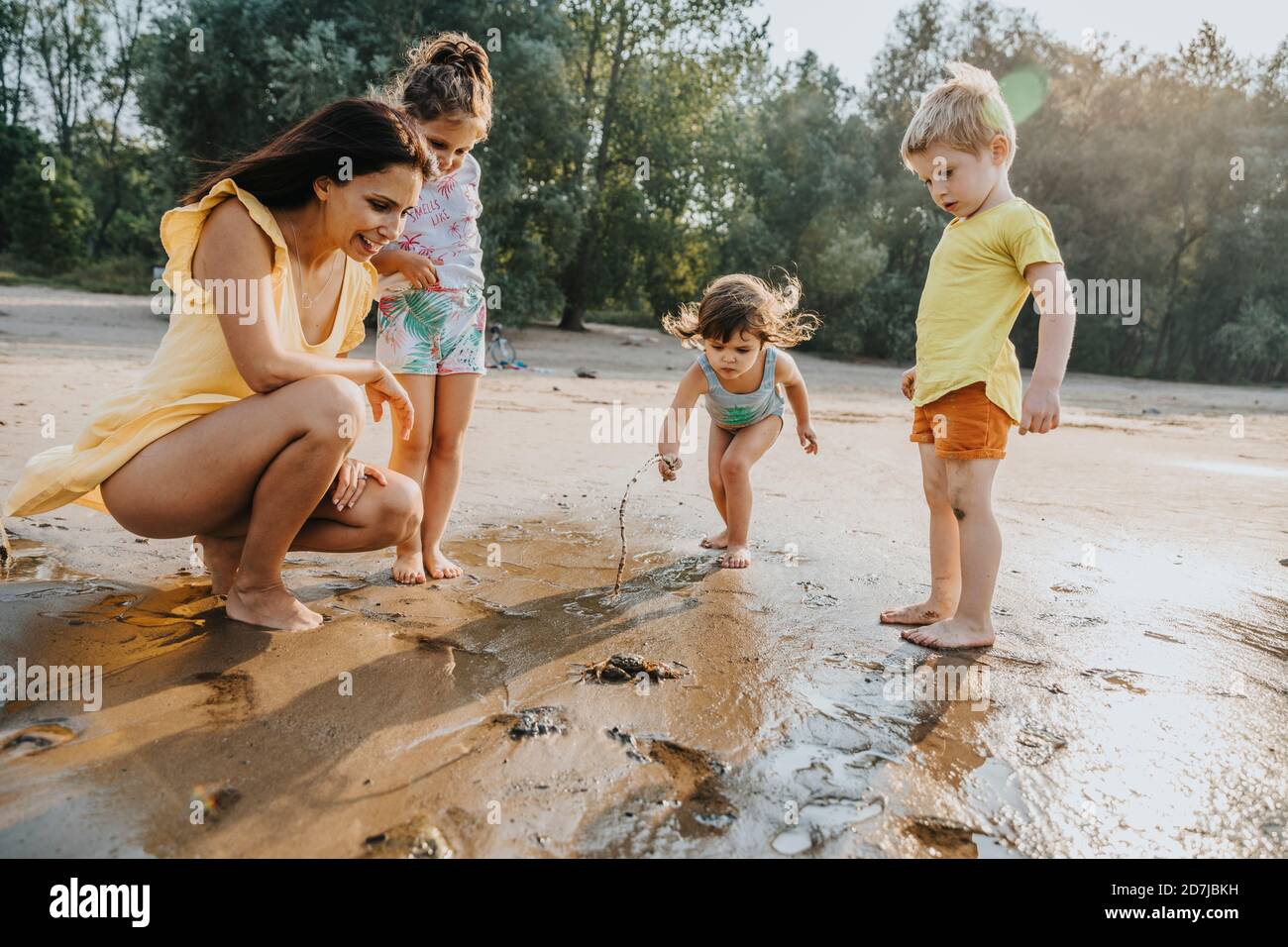 Mujer madura y niños descubriendo cangrejo en la playa Foto de stock