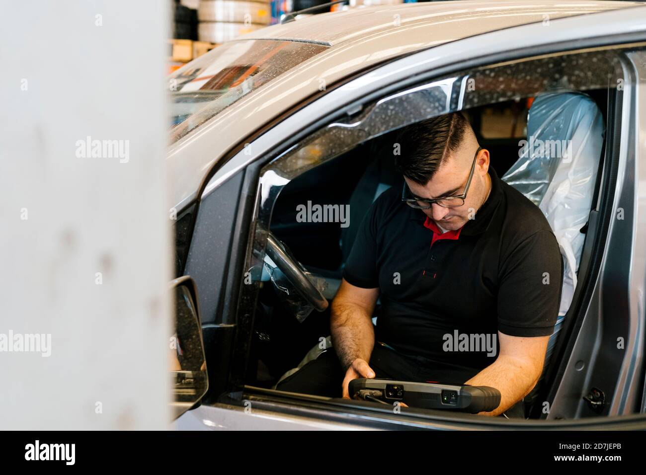 Mecánico que examina el auto mientras está sentado en el asiento del vehículo en el garaje Foto de stock