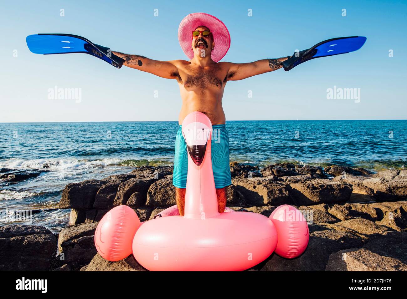 Hombre alegre usando una volteadora de buceo en la mano mientras está de pie anillo de flamingo contra el cielo despejado Foto de stock