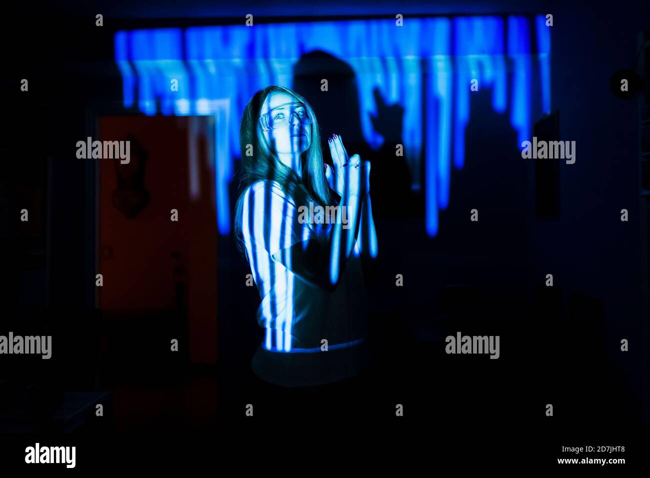 Mujer mostrando la señal de la mano de la pistola mientras está de pie en el reflejo de la luz en casa durante una pandemia Foto de stock