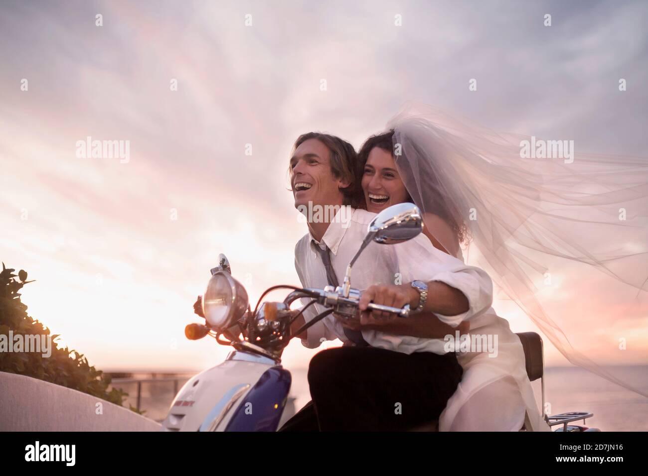 Alegre pareja recién vestida de boda en moto de motor durante puesta de sol  Fotografía de stock - Alamy