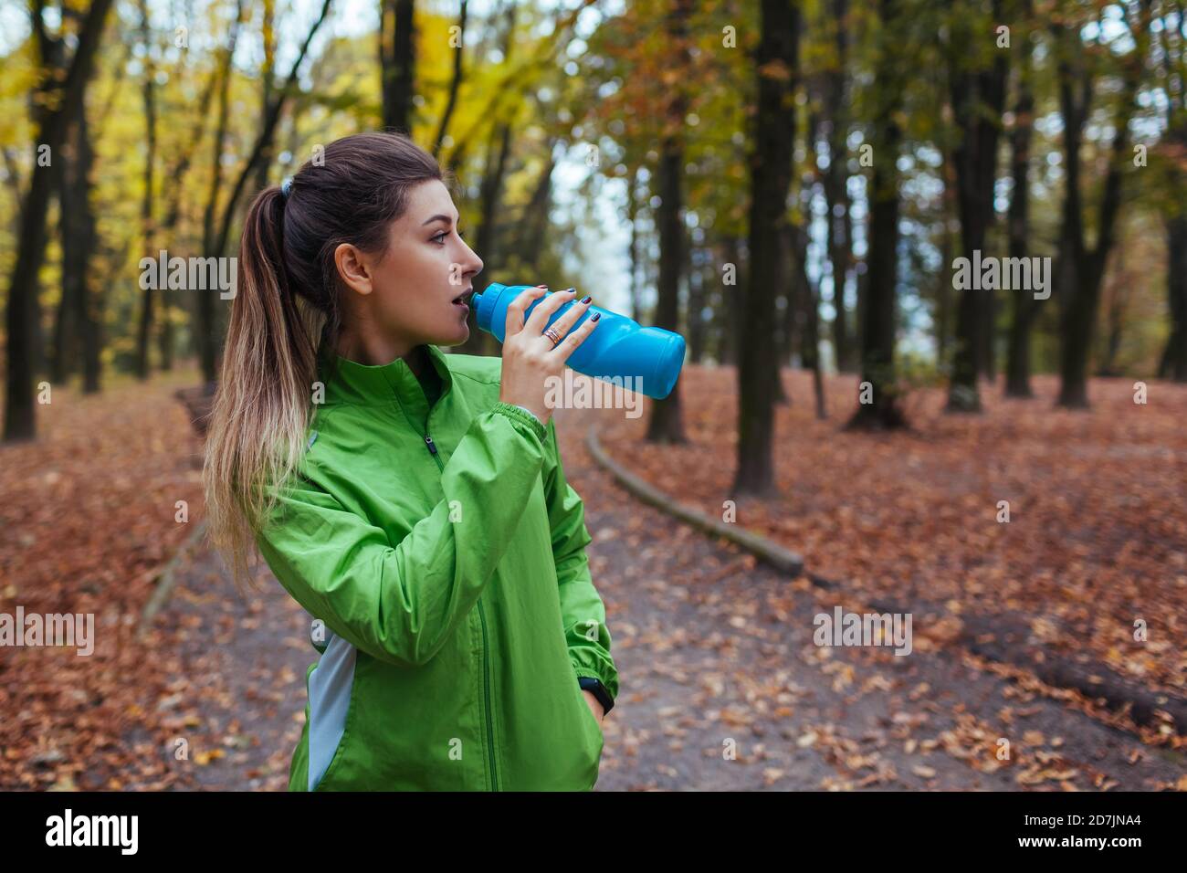 Corredor descansando después de entrenar en el parque de otoño. Mujer bebiendo agua. Estilo de vida activo deportivo Foto de stock