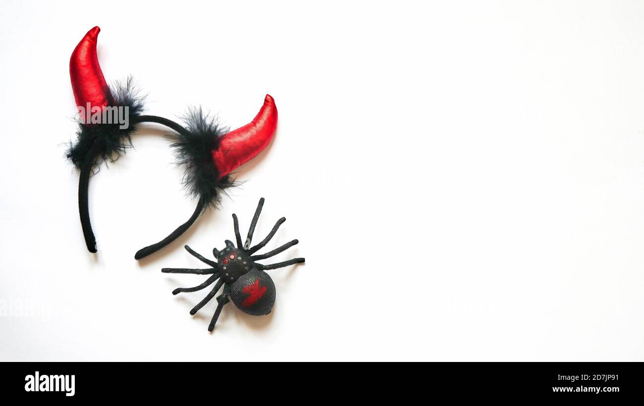 Rojo diablo cuernos cabeza aro y plástico juguete insecto araña negro sobre fondo blanco. Accesorio para la celebración de Halloween, vista superior, plano, espacio para copias Foto de stock