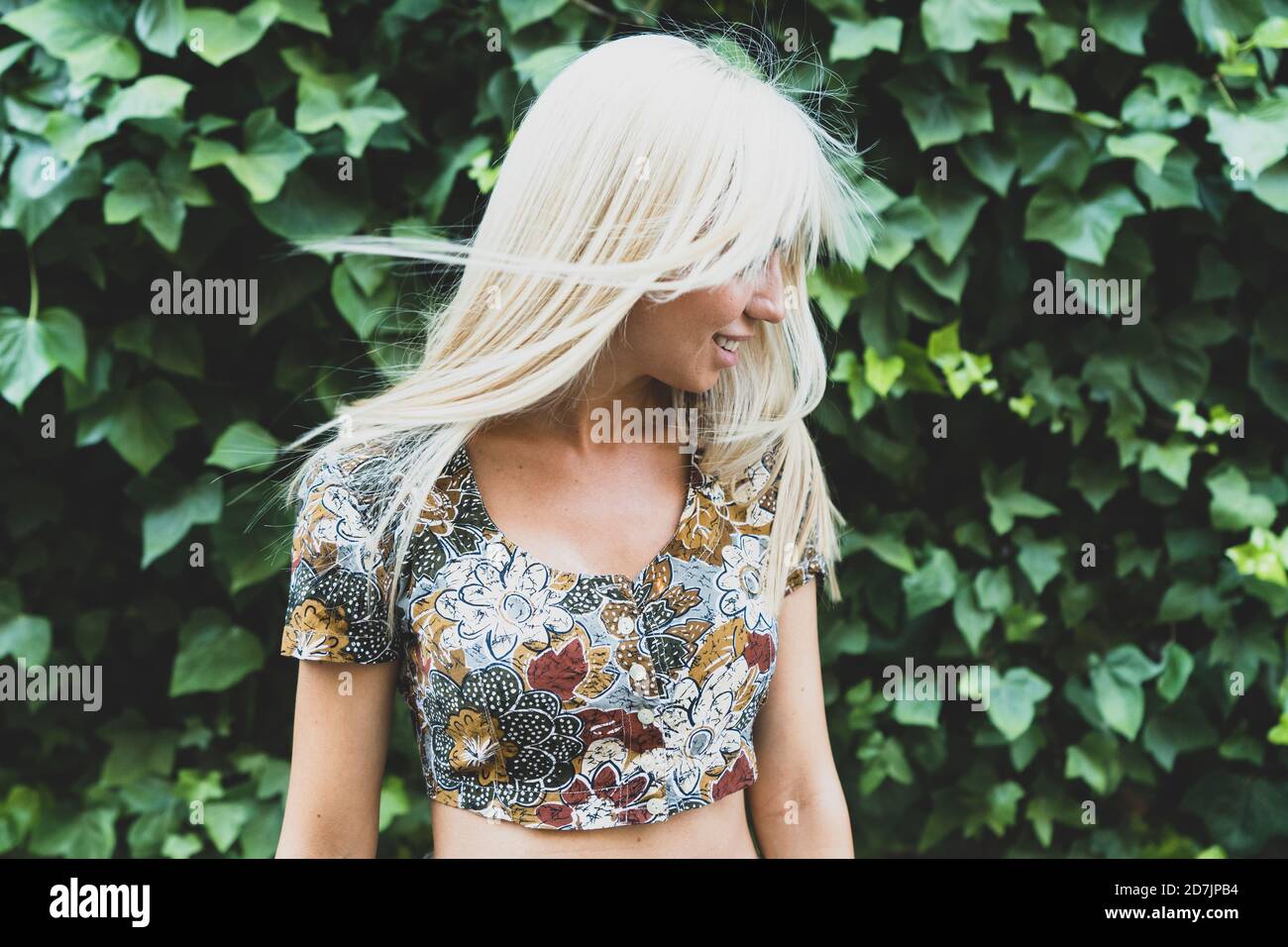 Sonriente mujer joven sacudiendo el cabello mientras está de pie contra las plantas en parque Foto de stock