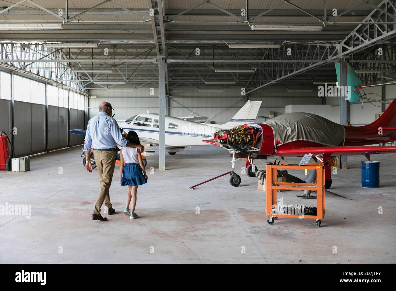Nieta y abuelo caminando en hangar de avión Foto de stock
