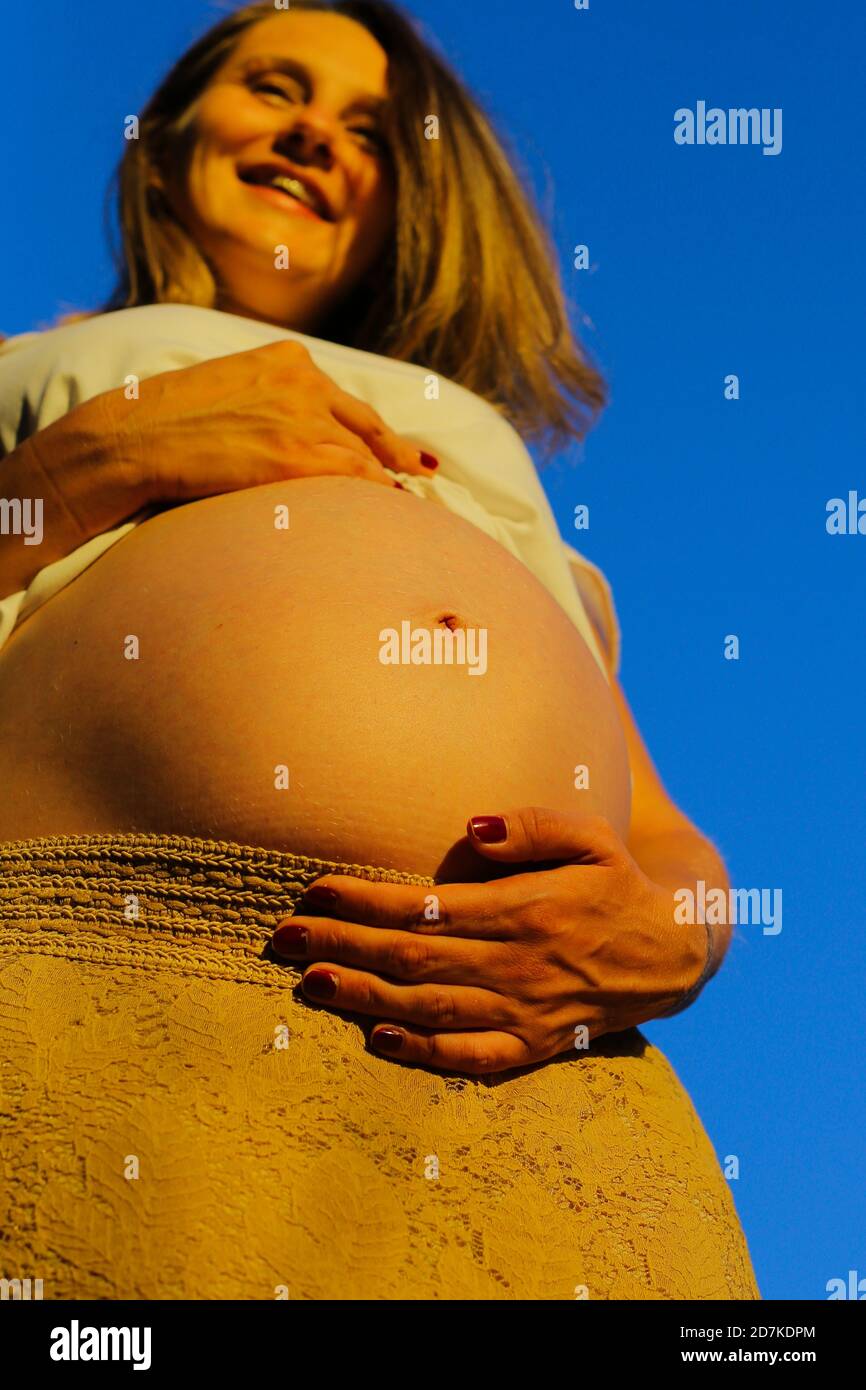 Tiro de ángulo bajo de una mujer embarazada feliz que la sostiene vientre  bajo la luz del sol Fotografía de stock - Alamy