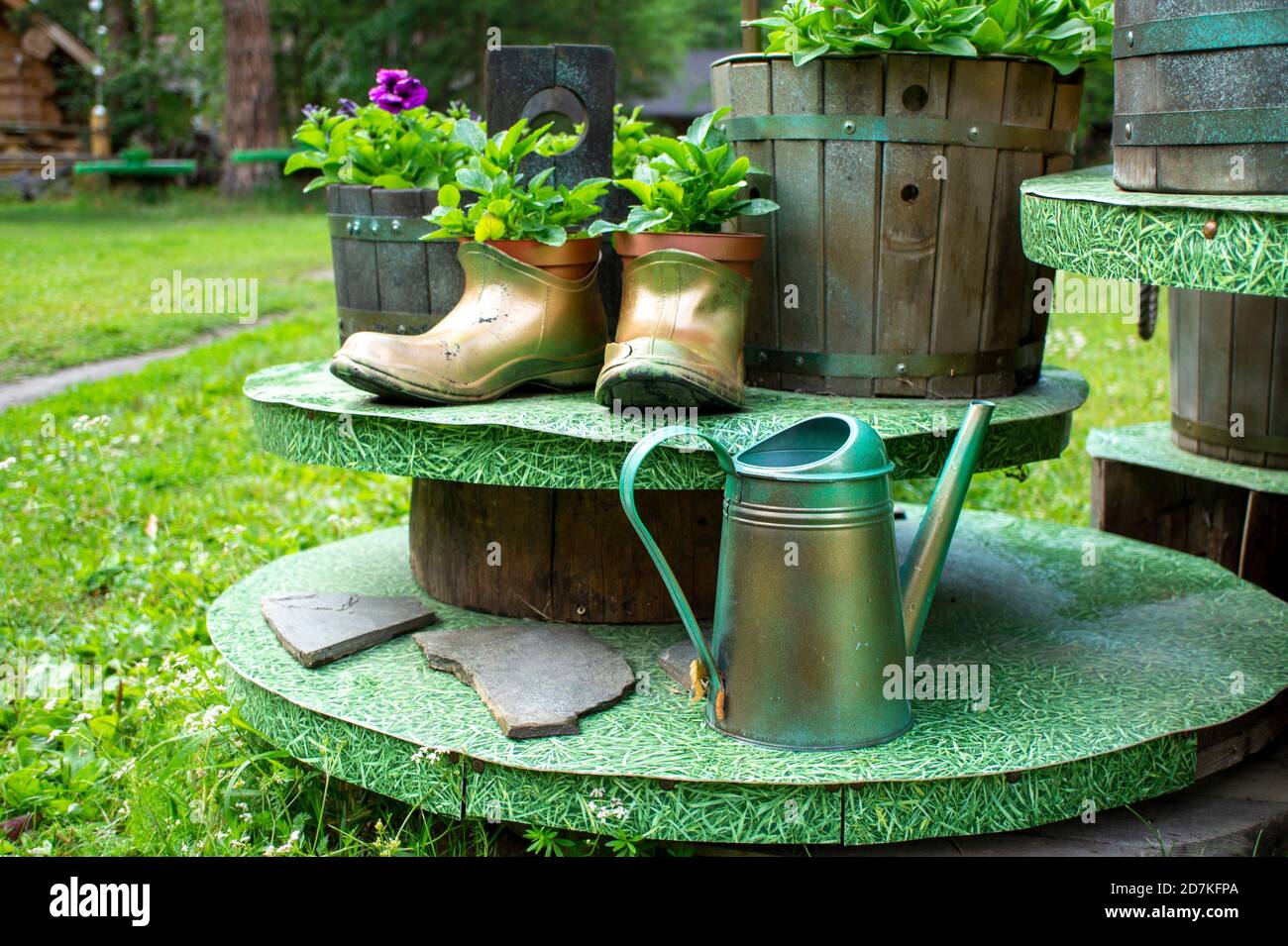 Maceta hecha a mano con botas de goma antiguas y macetas de madera y una lata de riego de metal en el jardín de verano. Concepto ecológico, diseño ecológico Foto de stock
