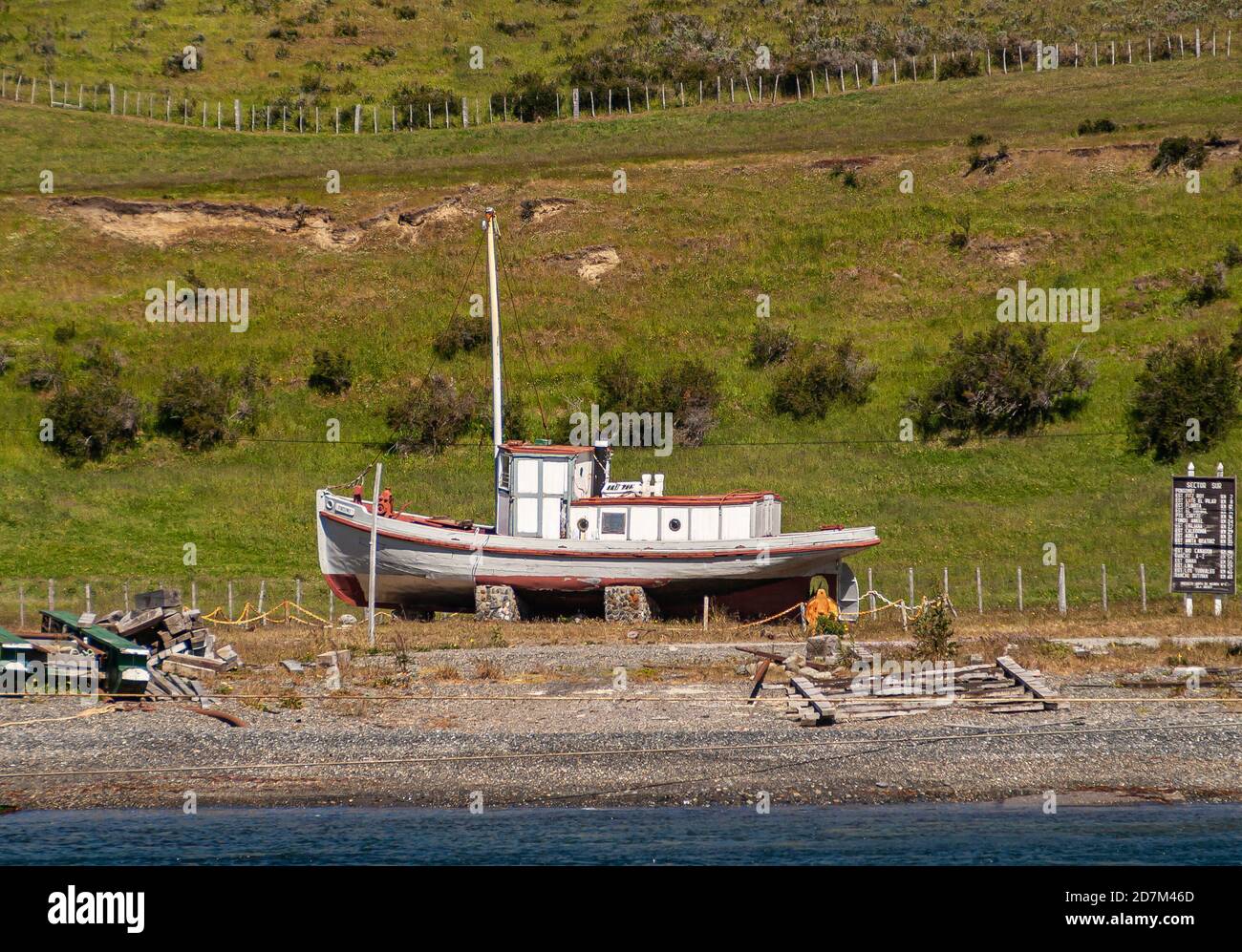 Isla Riesco, Chile - 12 de diciembre de 2008: El barco, previamente pintado de rojo y blanco, se encuentra en tierra verde frente a la playa Otway Sound y wa Foto de stock