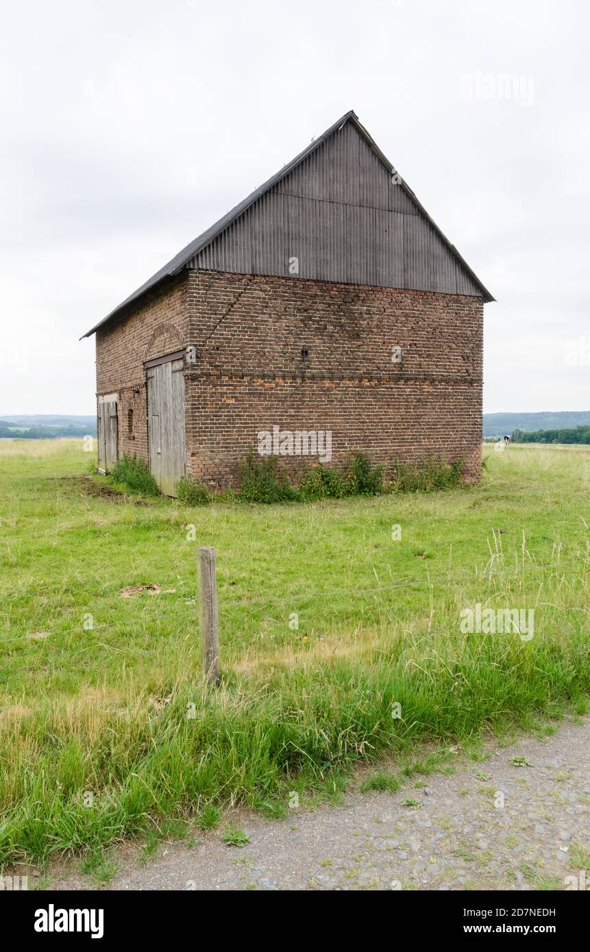 Granero abandonado hecho de ladrillos rojos con puertas de madera en un campo agrícola de hierba el campo rural, Alemania, Europa Occidental Foto de stock