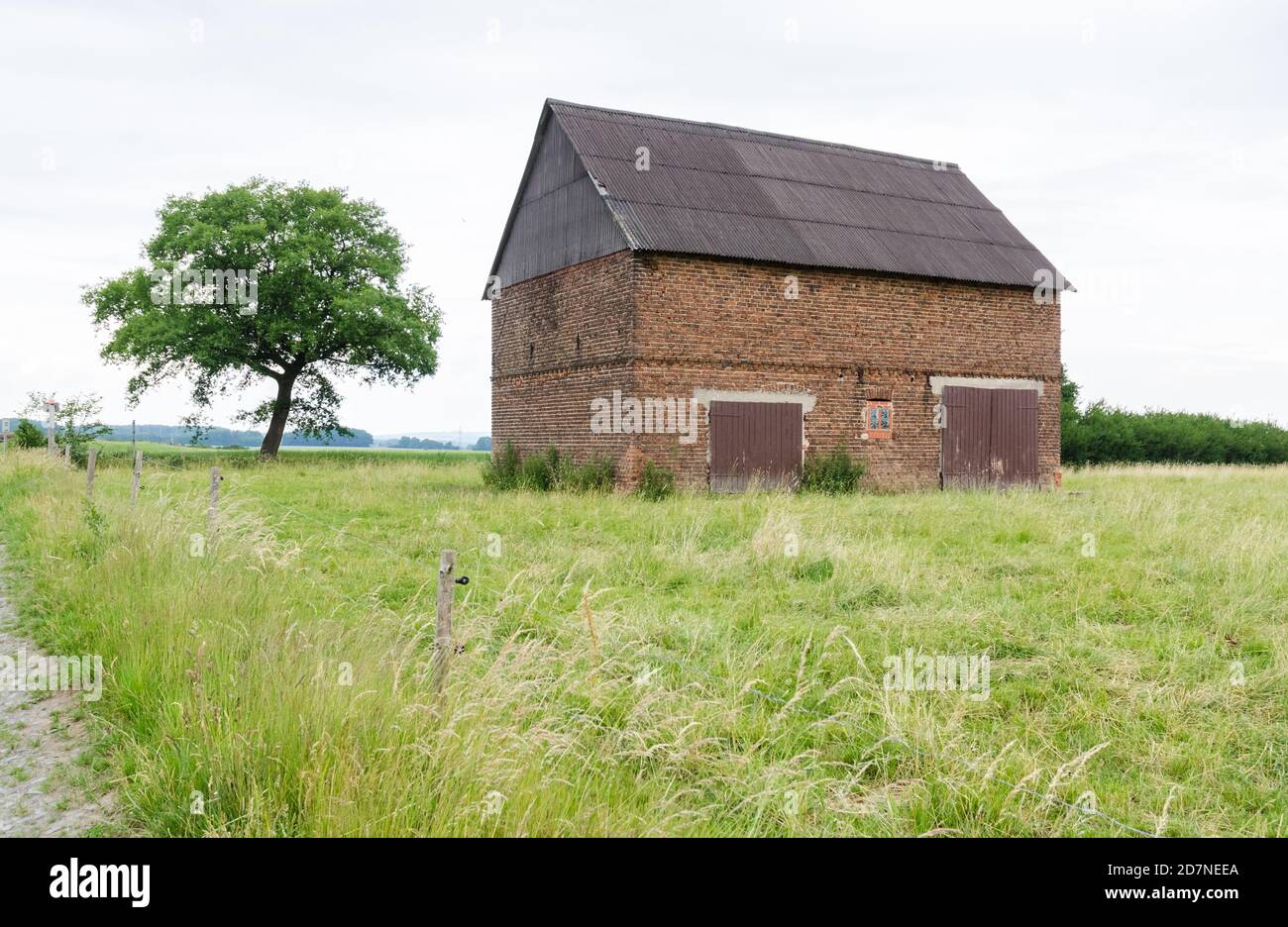 Granero abandonado hecho de ladrillos rojos con puertas de madera en un campo agrícola de hierba el campo rural, Alemania, Europa Occidental Foto de stock