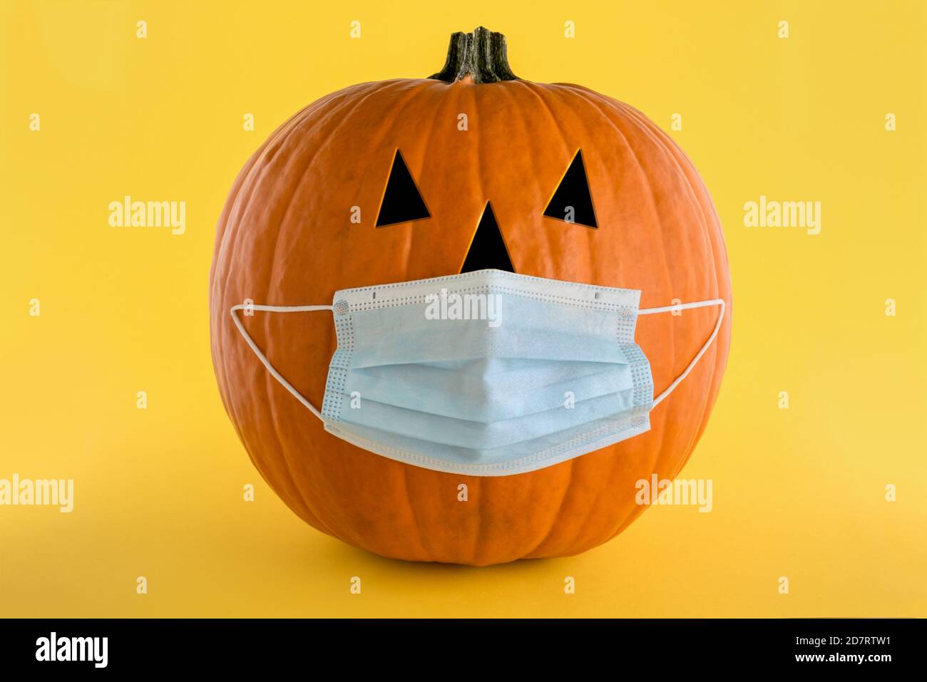 Calabaza de Halloween con una máscara médica para la protección del coronavirus (covid-19) Sobre un fondo amarillo.concepto de protección Foto de stock