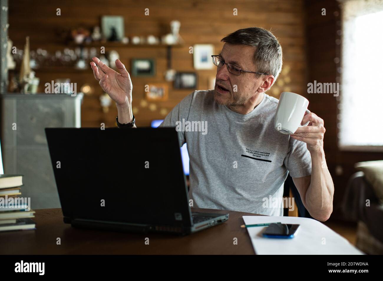 Un hombre medio adulto sosteniendo una taza discutiendo usando una videoconferencia. Foto de stock