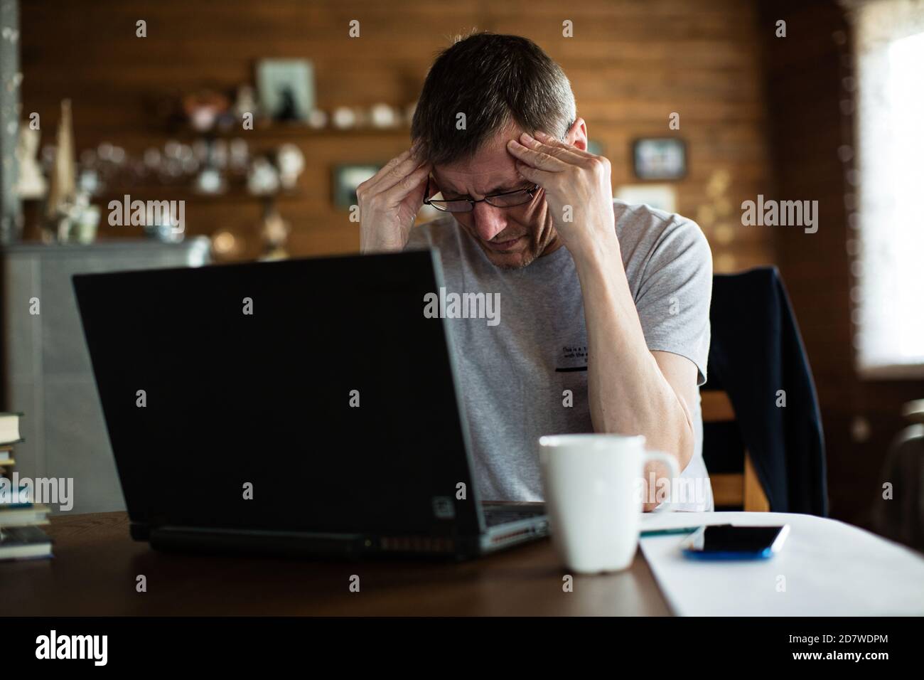 Frustrado hombre medio adulto tocando la cabeza y manteniendo los ojos cerrados mientras estaba sentado frente al portátil. Foto de stock