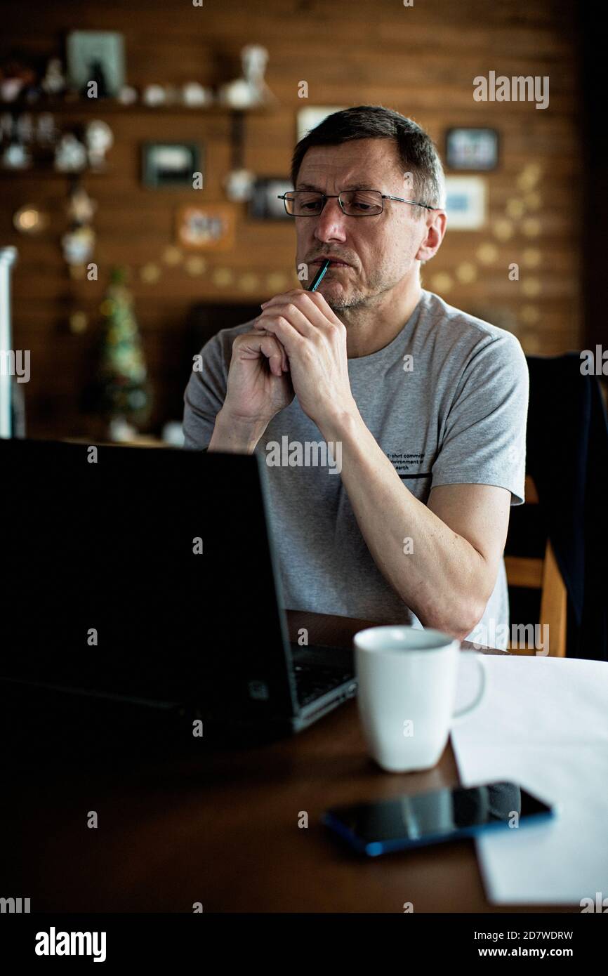 Hombre medio adulto sentado en la mesa y mirando el portátil. Foto de stock