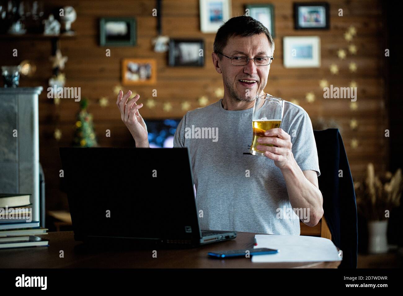 Hombre medio adulto mirando el portátil y sosteniendo un vaso de cerveza y sonriendo. Concepto de fiesta en línea. Foto de stock