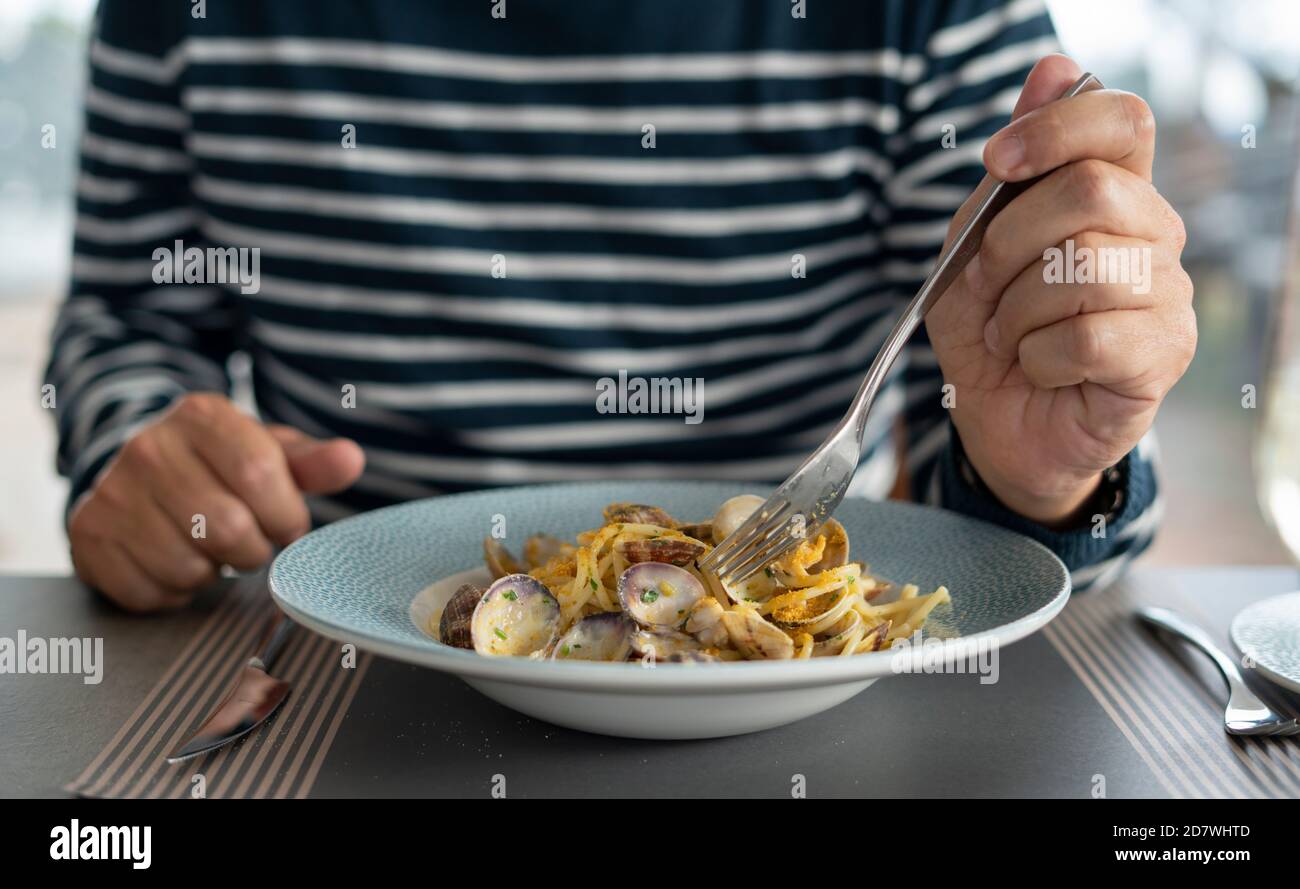 Detalle macho comer a mano pasta espaguetis con almejas y salmonetes, comida mediterránea Foto de stock